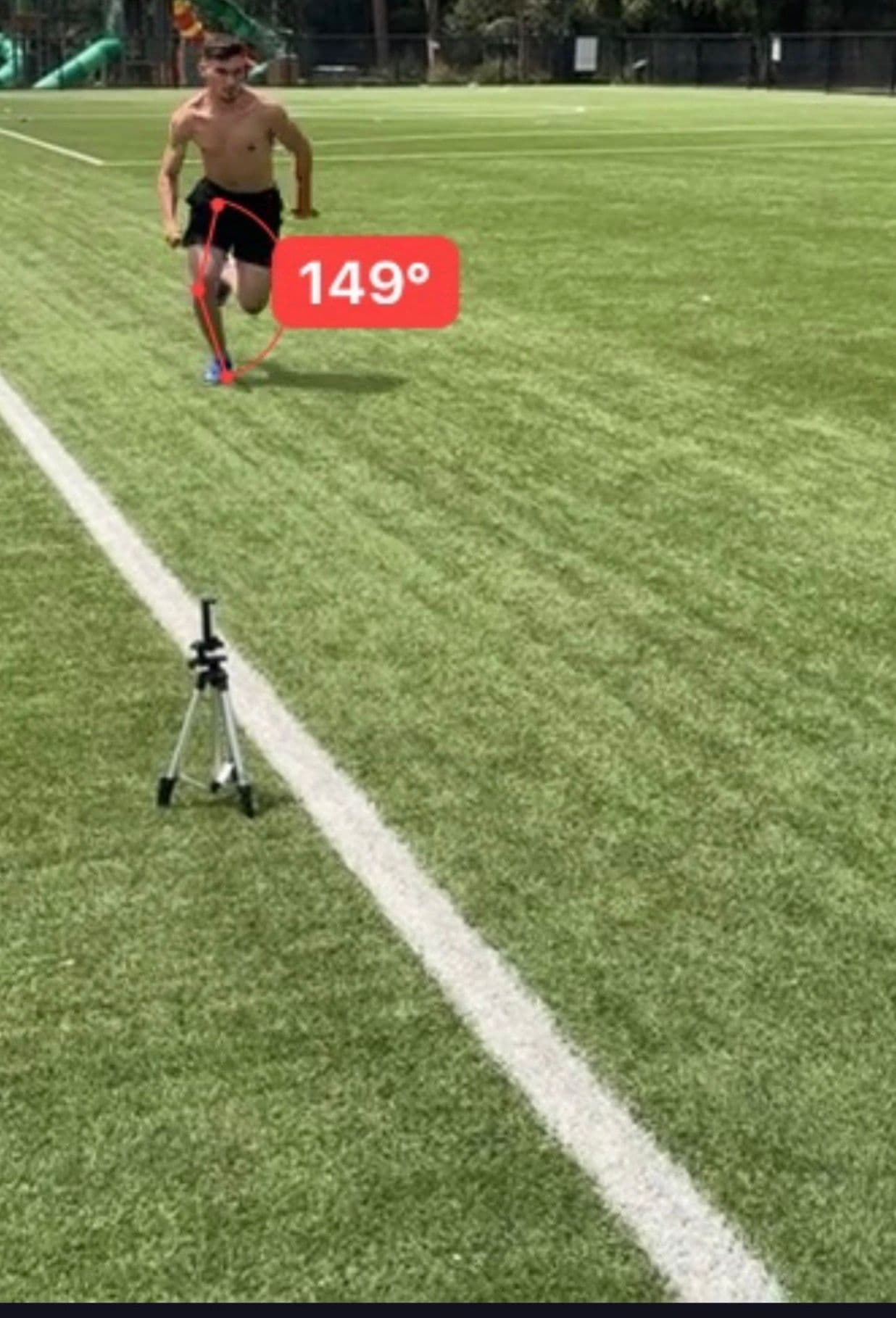 Athlete sprinting toward a tripod-mounted camera on the white line — knee-angle annotation at 149° overlaid on the leading leg